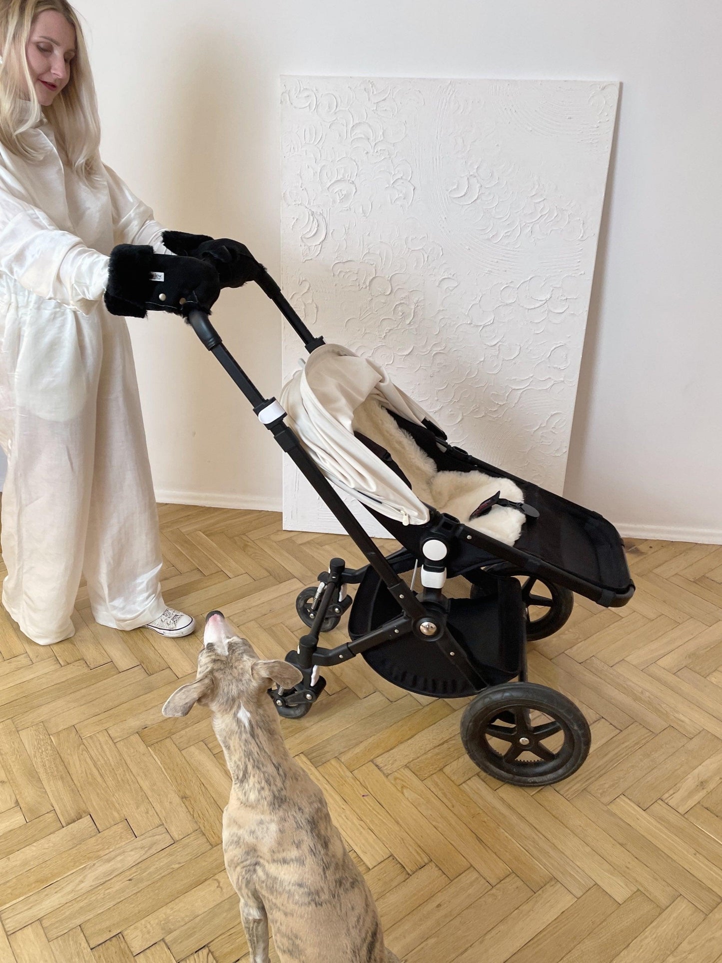 A woman standing next to a stroller with a dog covered in MellowConceptStore's Waterproof Natural Sheepskin Stroller Hand Muffs - Black&White.