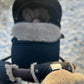 A person's hand holding a MellowConceptStore Waterproof Natural Sheepskin Stroller Hand Muffs - Black&White in the snow.