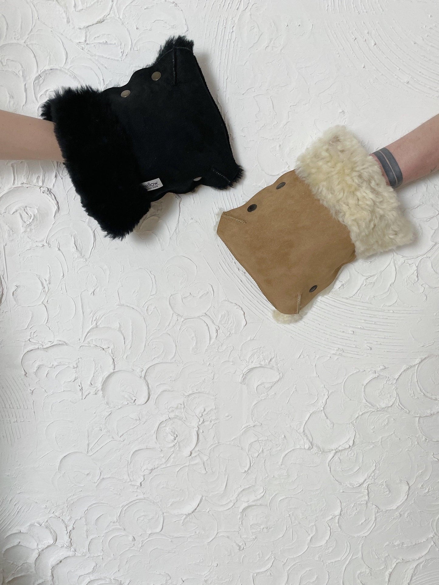 A pair of Waterproof Natural Sheepskin Stroller Hand Muffs - Black&White from MellowConceptStore hanging on a white wall.