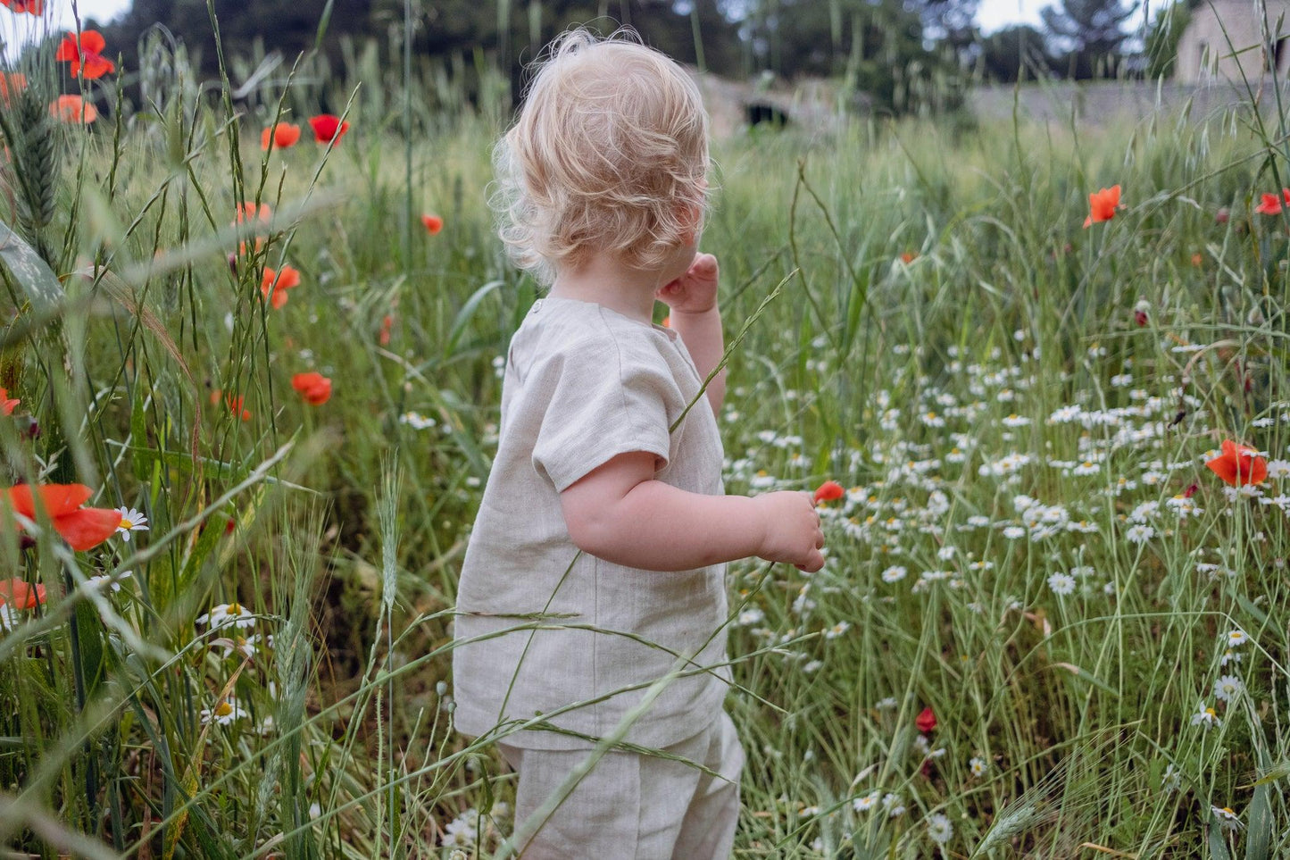 A child walking through a field of Ramie Baby/Kid Clothing Set - Beige by Mellow Concept Store flowers.