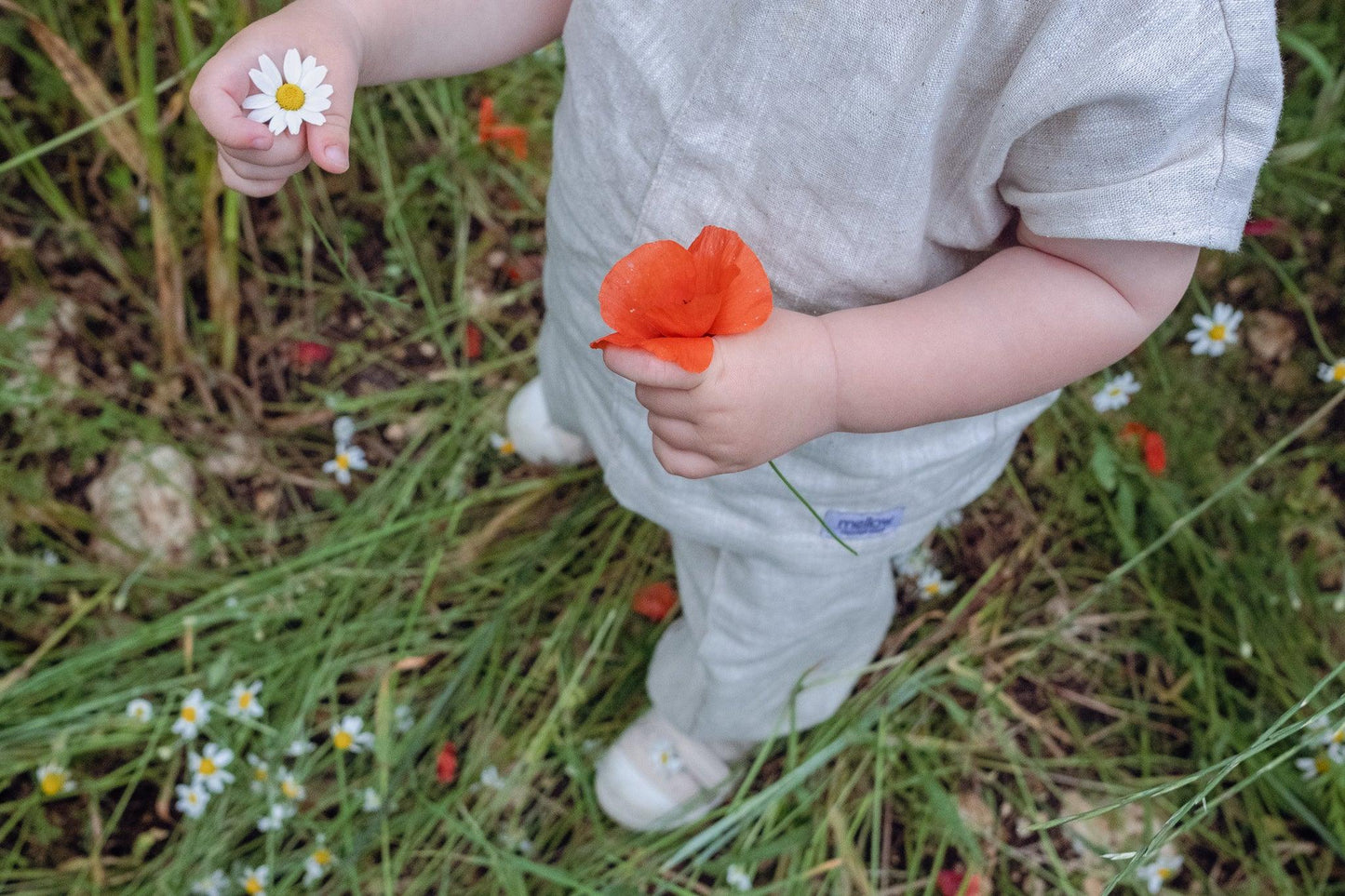 A baby is standing in a sustainable field of flowers wearing the Ramie Baby/Kid Clothing Set in Beige from Mellow Concept Store.