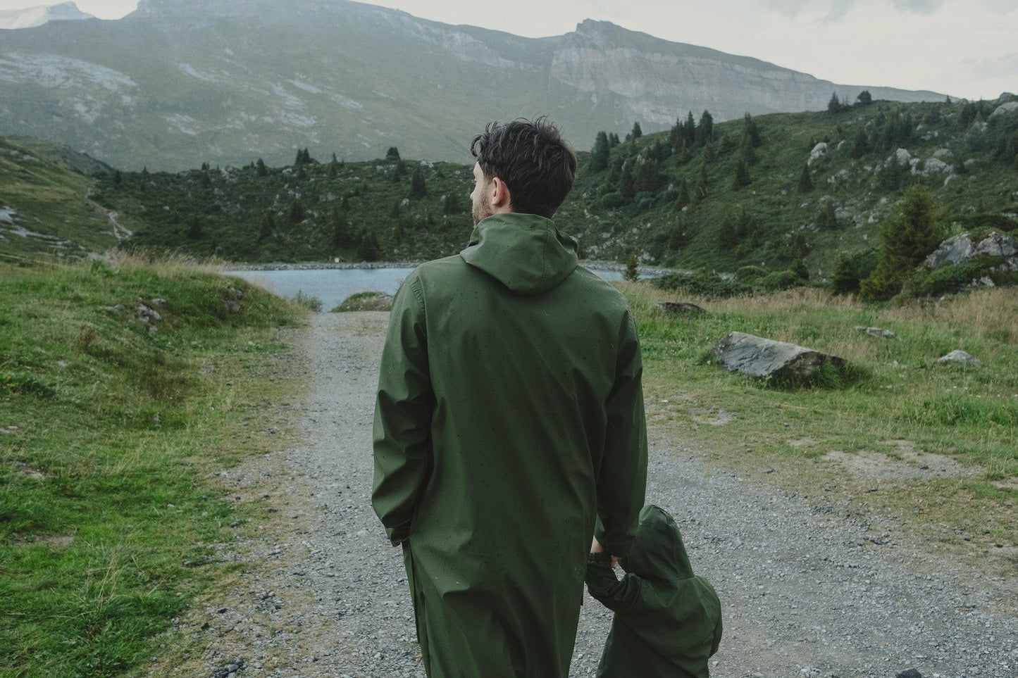 A person in a green, Waterproof Baby/Kid Clothing Set - Khaki from MellowConceptStore walking towards a lake with mountains in the background.