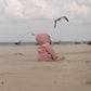 A child in the MellowConceptStore Waterproof Baby/Kid Clothing Set - Rosa sits alone on a sandy beach, gazing at a seagull flying by, with more seagulls and a cloudy sky in the background.