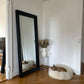 An Oval Natural Sheepskin Pet Bed from Mellow Pet Store in front of a mirror in a room.