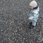 A young child wearing a light-colored merino wool winter hat and a Waterproof Baby/Kid Clothing Set - Silver from MellowConceptStore stands on a gravel surface, looking to the side.