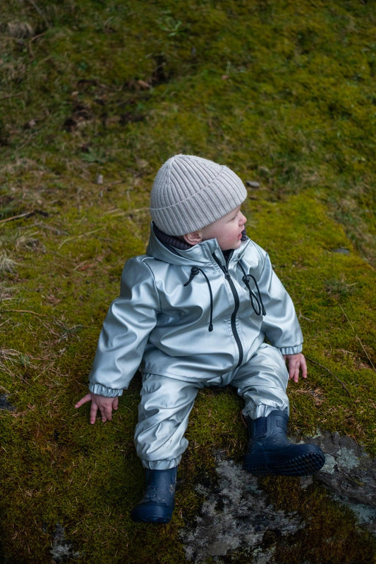 A toddler in a Waterproof Baby/Kid Clothing Set in silver from MellowConceptStore sits on a moss-covered rock, looking off to the side.