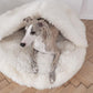 A greyhound dog lounging in a fluffy Natural Sheepskin Pet Cave - White made from Mellow Pet Store.