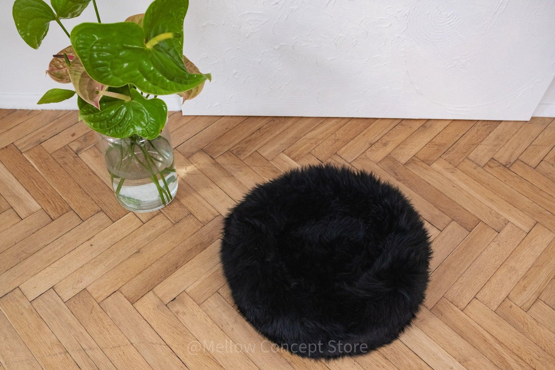 An Round Natural Sheepskin Pet Bed - Black on a wooden floor.