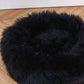 A Round Natural Sheepskin Pet Bed - Black from Mellow Pet Store on a wooden floor.