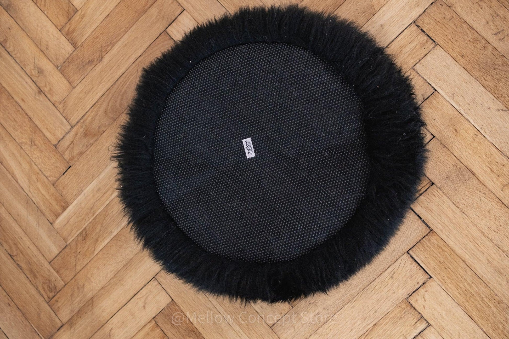 A round black fur rug on a wooden floor made from Mellow Pet Store's Round Natural Sheepskin Pet Bed in Black, creating an eco-friendly and luxurious addition to any room.