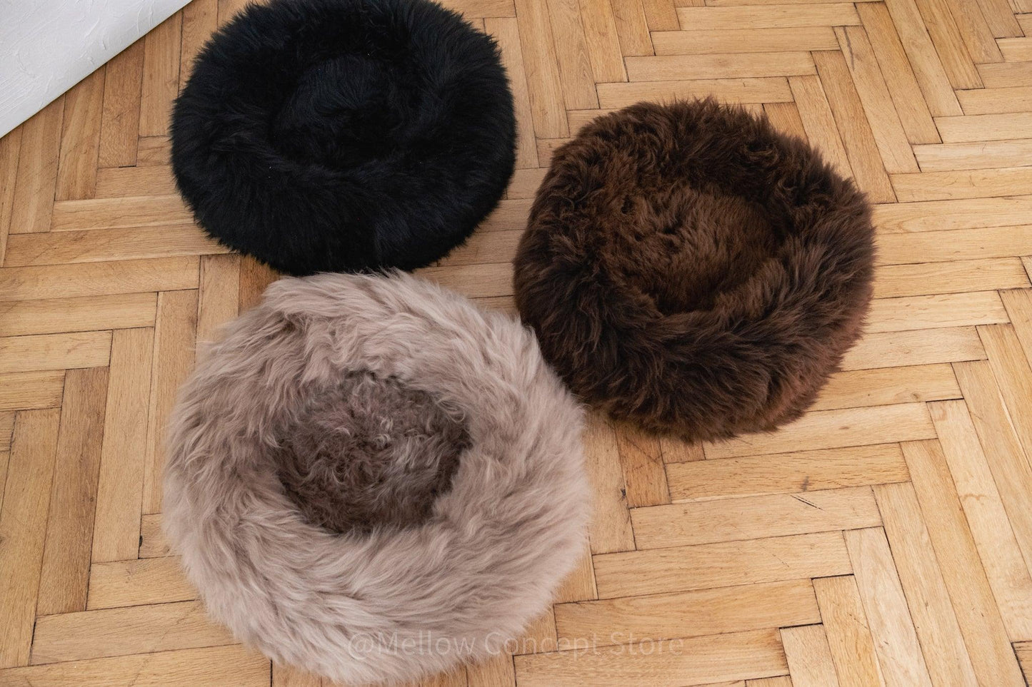 Three Round Natural Sheepskin Pet Beds - Black from Mellow Pet Store on a wooden floor.