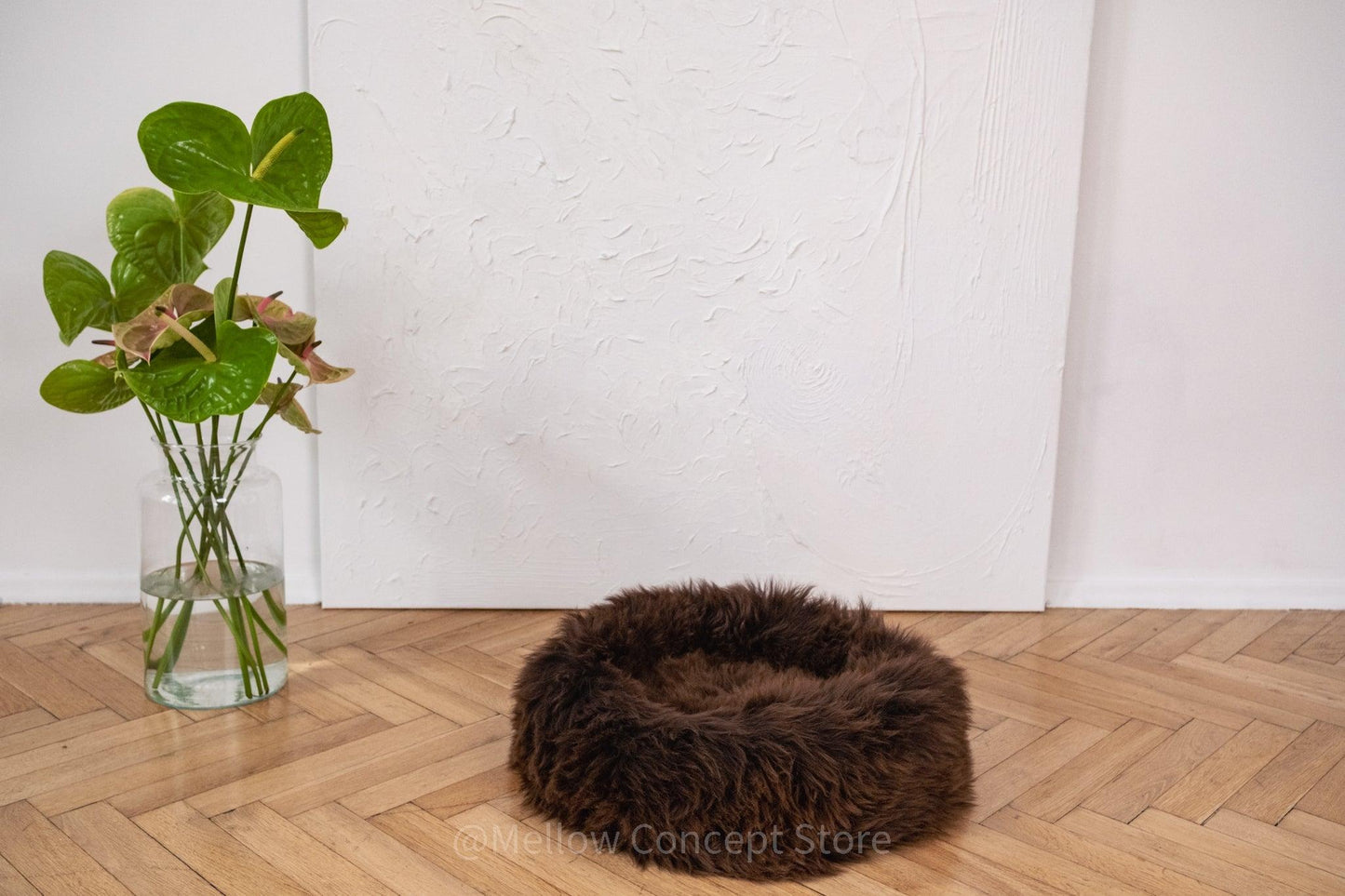 A Round Natural Sheepskin Pet Bed in brown, eco-friendly and hypoallergenic, lays on a wooden floor from Mellow Pet Store.