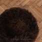 An organic Round Natural Sheepskin Pet Bed - Brown from Mellow Pet Store on a wooden floor.