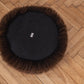 A black fur ball lounging on a wooden floor with Round Natural Sheepskin Pet Bed in Brown from Mellow Pet Store nearby.