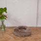 A Round Natural Sheepskin Pet Bed in Greige from Mellow Pet Store on a wooden floor made from sustainable materials.