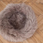 A Round Natural Sheepskin Pet Bed - Greige from Mellow Pet Store on a wooden floor, made from sustainable materials.