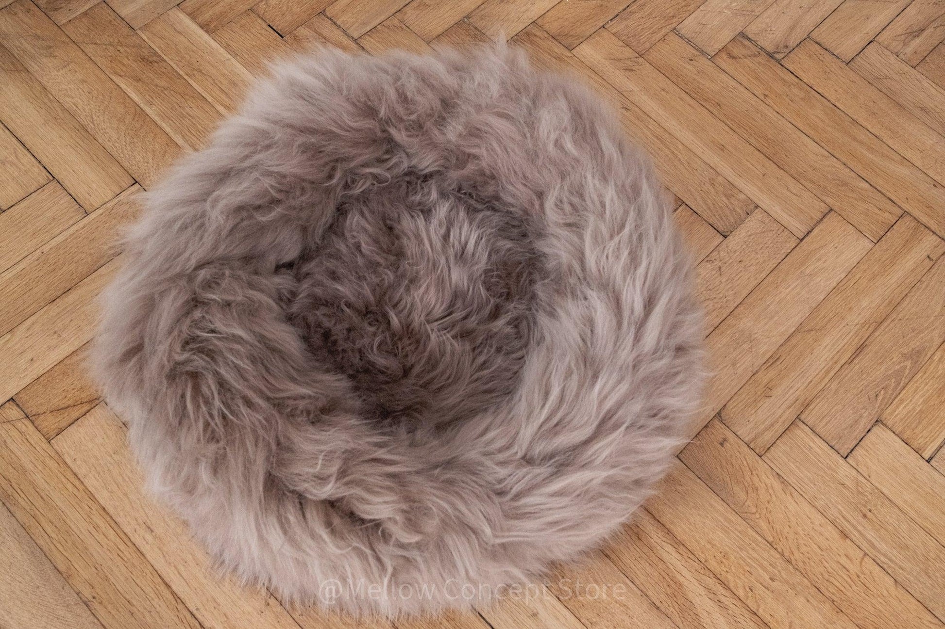 A Round Natural Sheepskin Pet Bed - Greige from Mellow Pet Store on a wooden floor, made from sustainable materials.