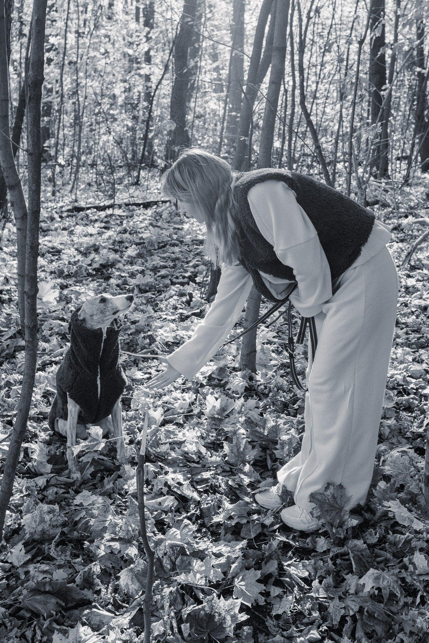 A woman is petting a Woolen Dog Vest - Charcoal by Mellow Pet Store in the woods.