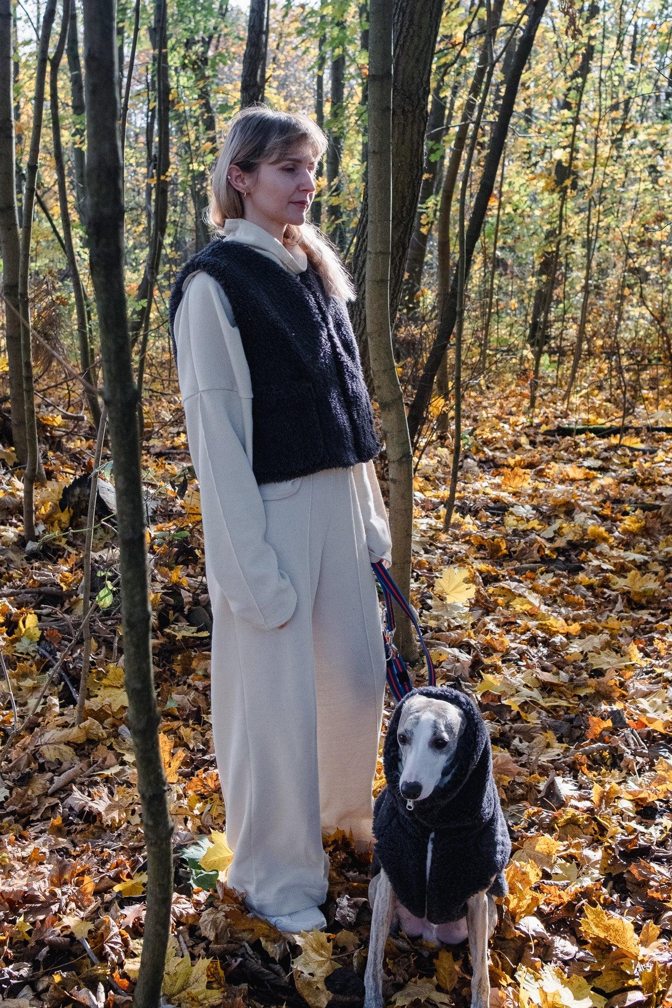 A woman standing next to a Woolen Dog Vest - Charcoal from Mellow Pet Store in the eco-friendly woods.