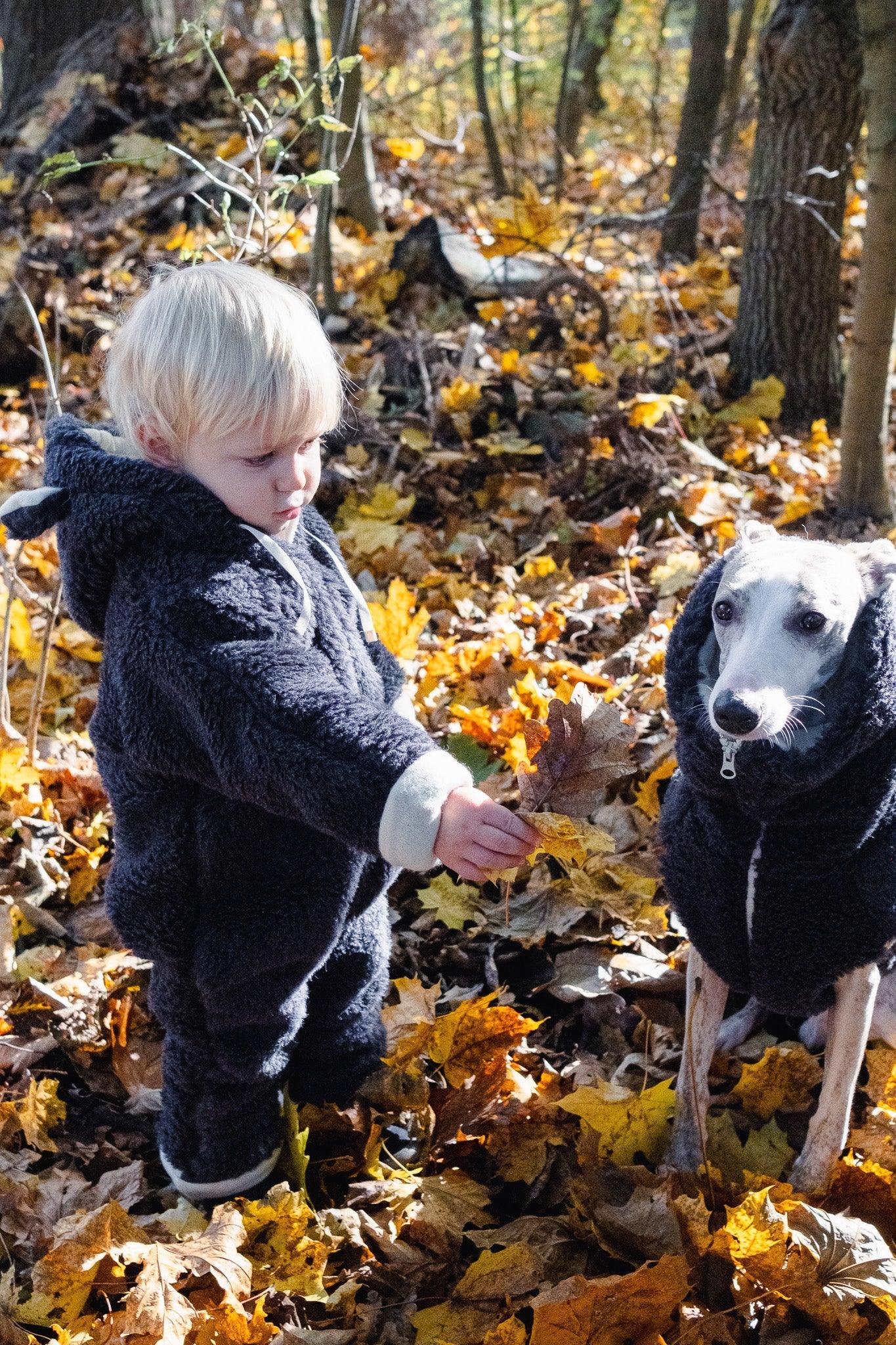 A little boy and a Mellow Pet Store Woolen Dog Vest - Charcoal in the natural woods.