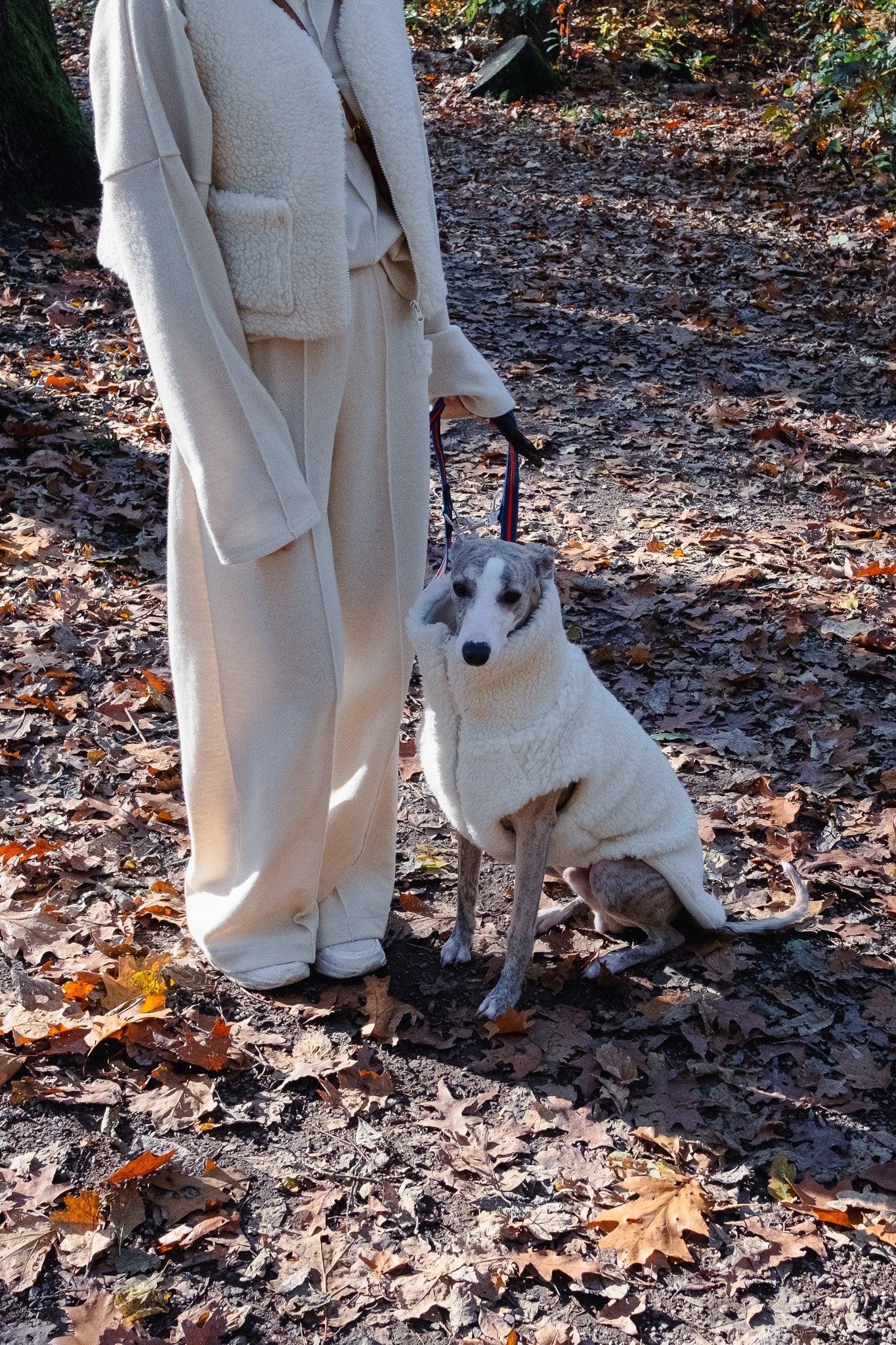 A woman with a Mellow Pet Store woolen dog vest in white standing in the woods, enjoying the natural surroundings.