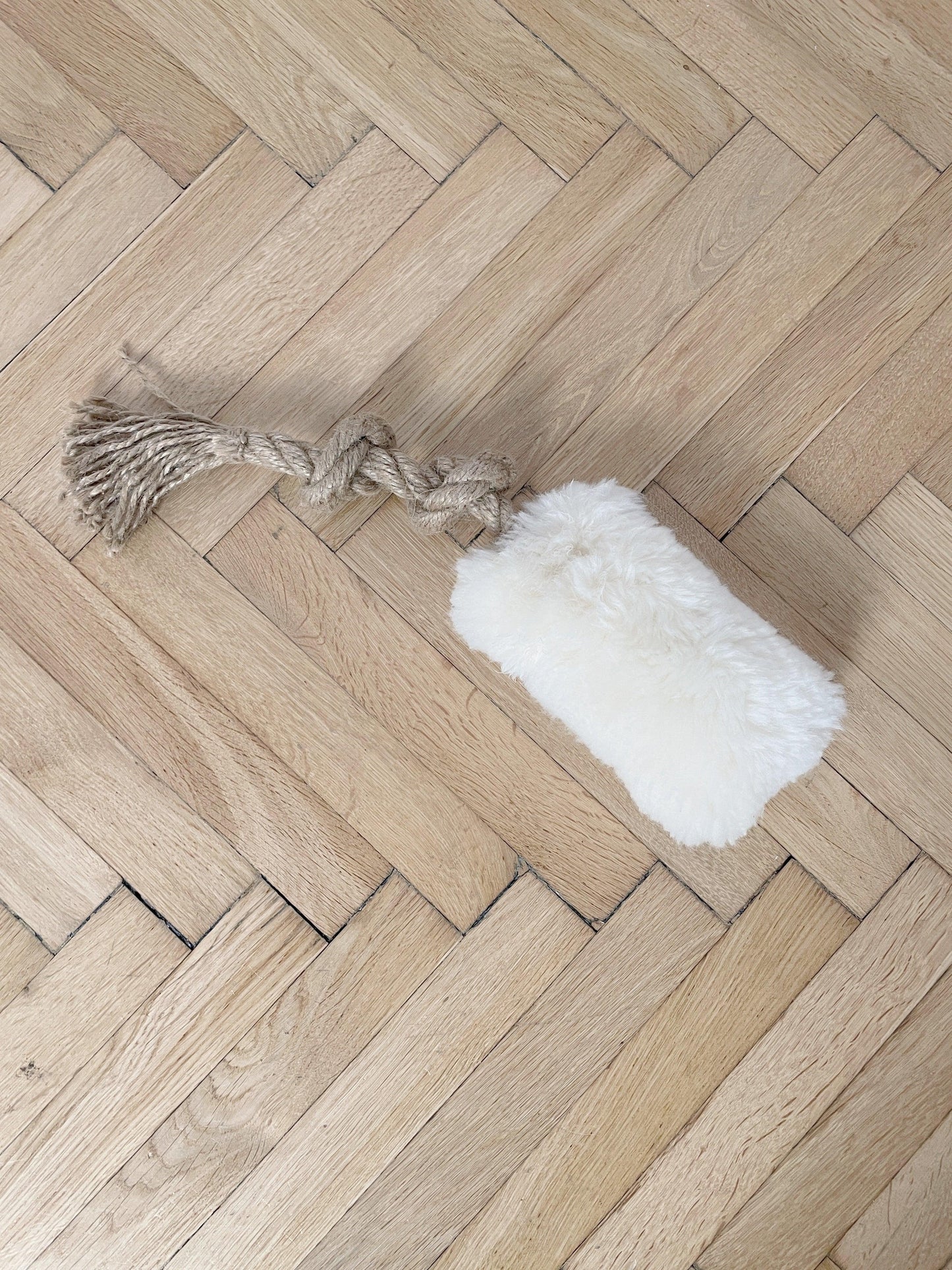 A white Natural Sheepskin Dog Tug Toy from Mellow Pet Store is placed on a wooden floor, offering a touch of eco-luxury in pet care.