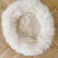 An organic Round Natural Sheepskin Pet Bed from Mellow Pet Store on a wooden floor.