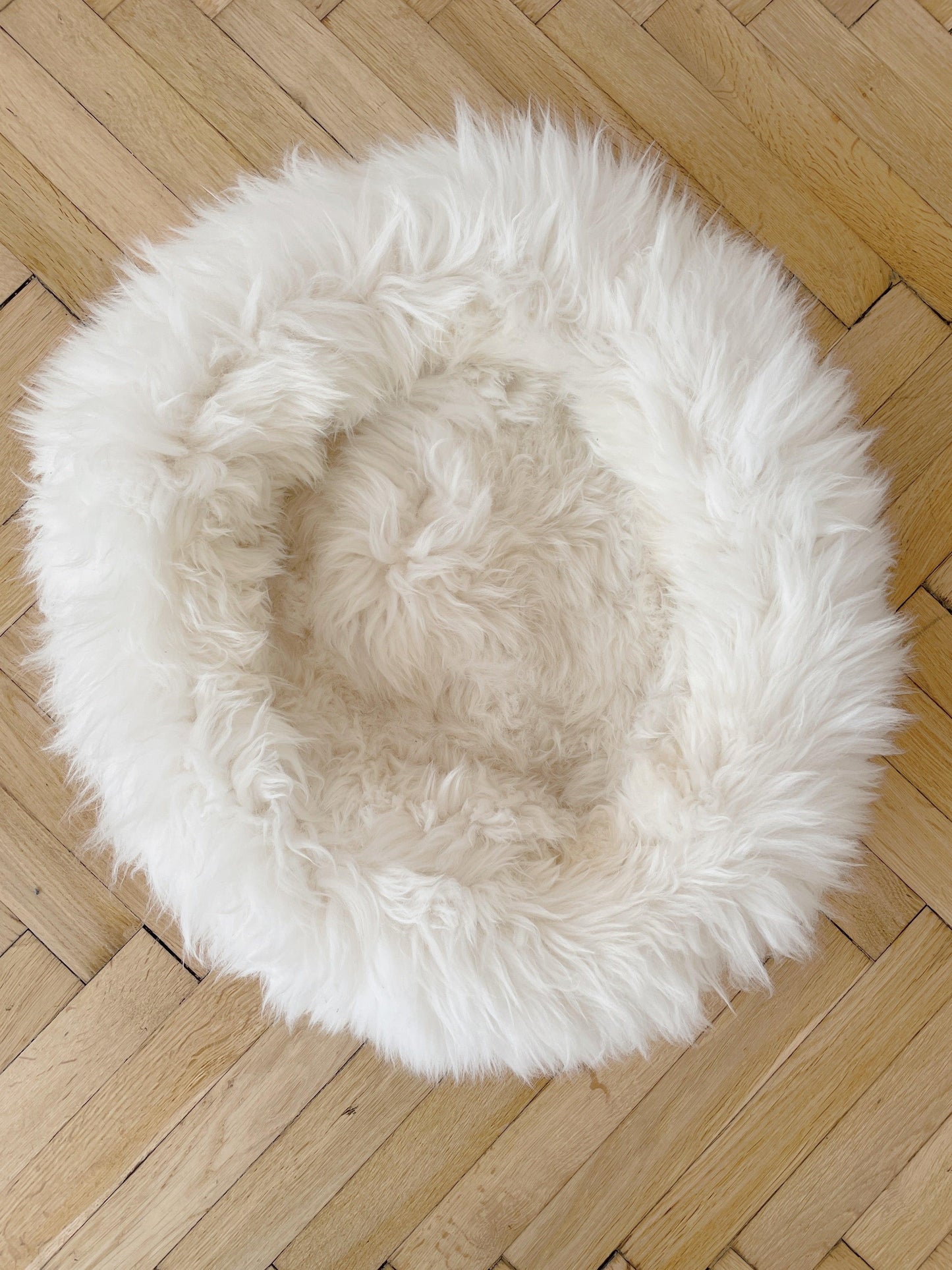 An organic Round Natural Sheepskin Pet Bed from Mellow Pet Store on a wooden floor.