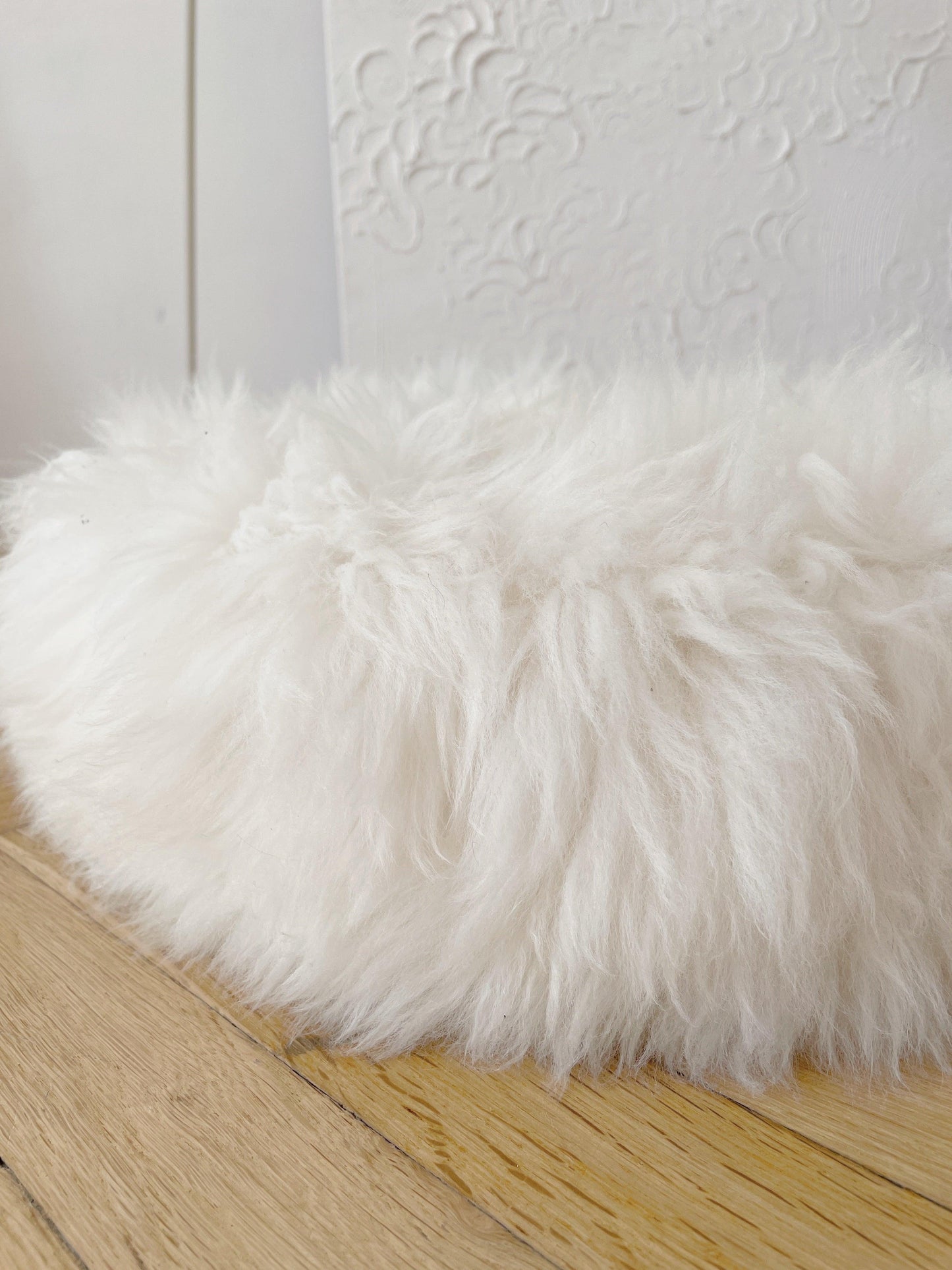 A Round Natural Sheepskin Pet Bed from Mellow Pet Store on a wooden floor, made of natural sheepskin.