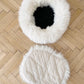 A white and black Round Natural Sheepskin Pet Bed from Mellow Pet Store on a wooden floor.