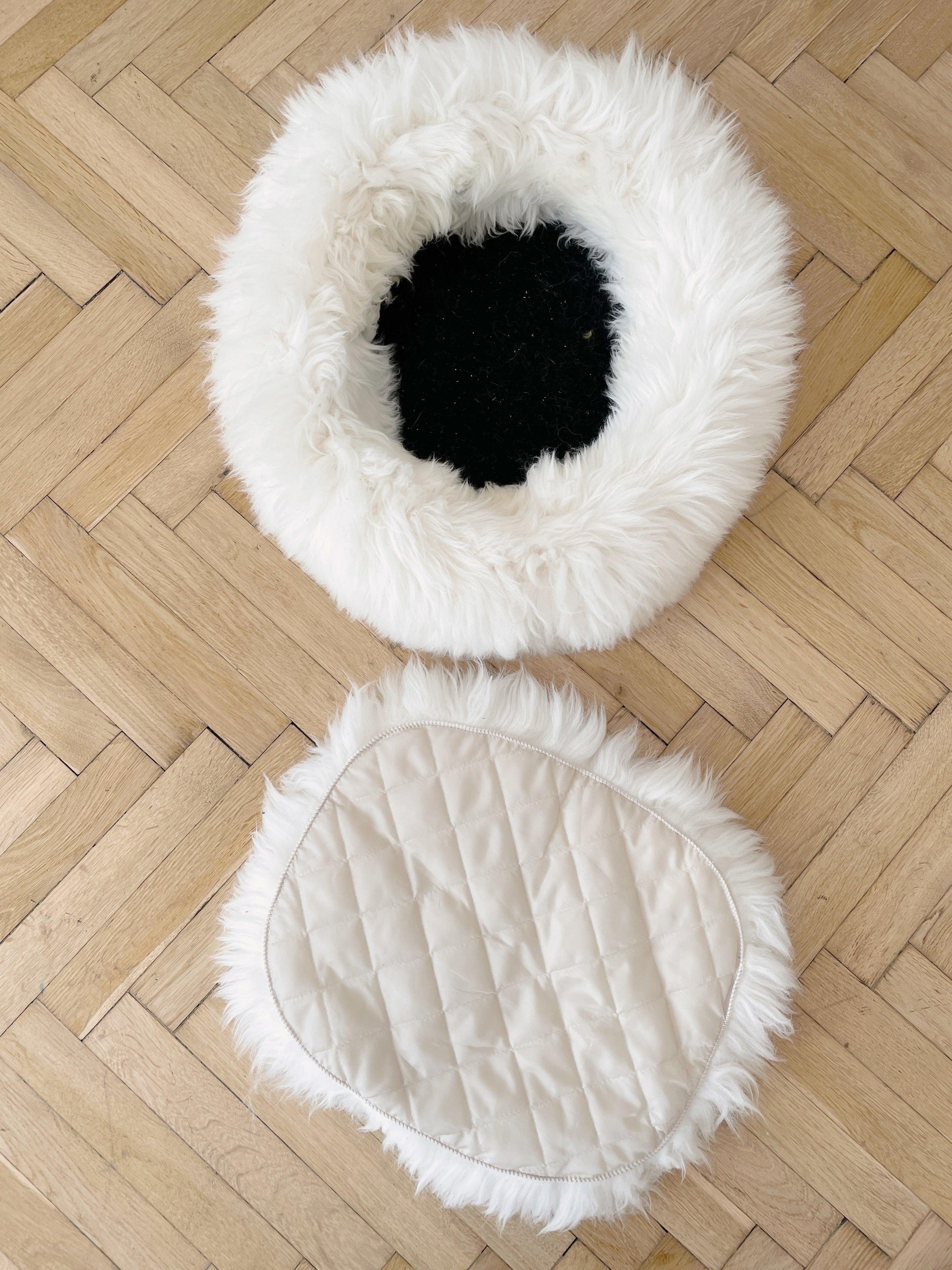 A white and black Round Natural Sheepskin Pet Bed from Mellow Pet Store on a wooden floor.