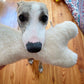 A dog is holding a Natural Sheepskin Dog Toy Bone near its Eco-luxury pet supplies from Mellow Pet Store.