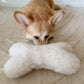A dog lounges on a rug with a Natural Sheepskin Dog Toy Bone from Mellow Pet Store.