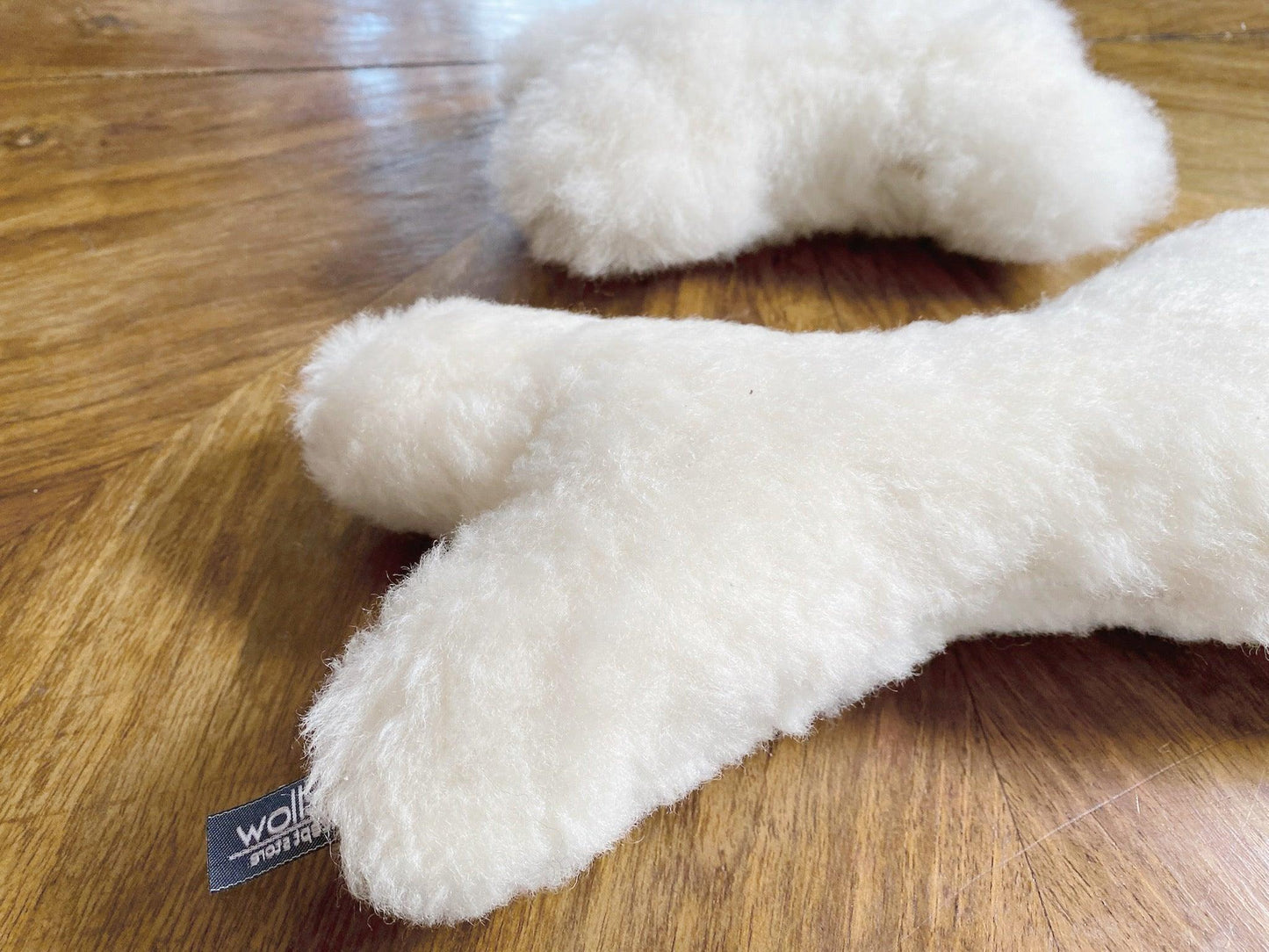 Two white Mellow Pet Store Natural Sheepskin Dog Toy Bones resting on a wooden floor.