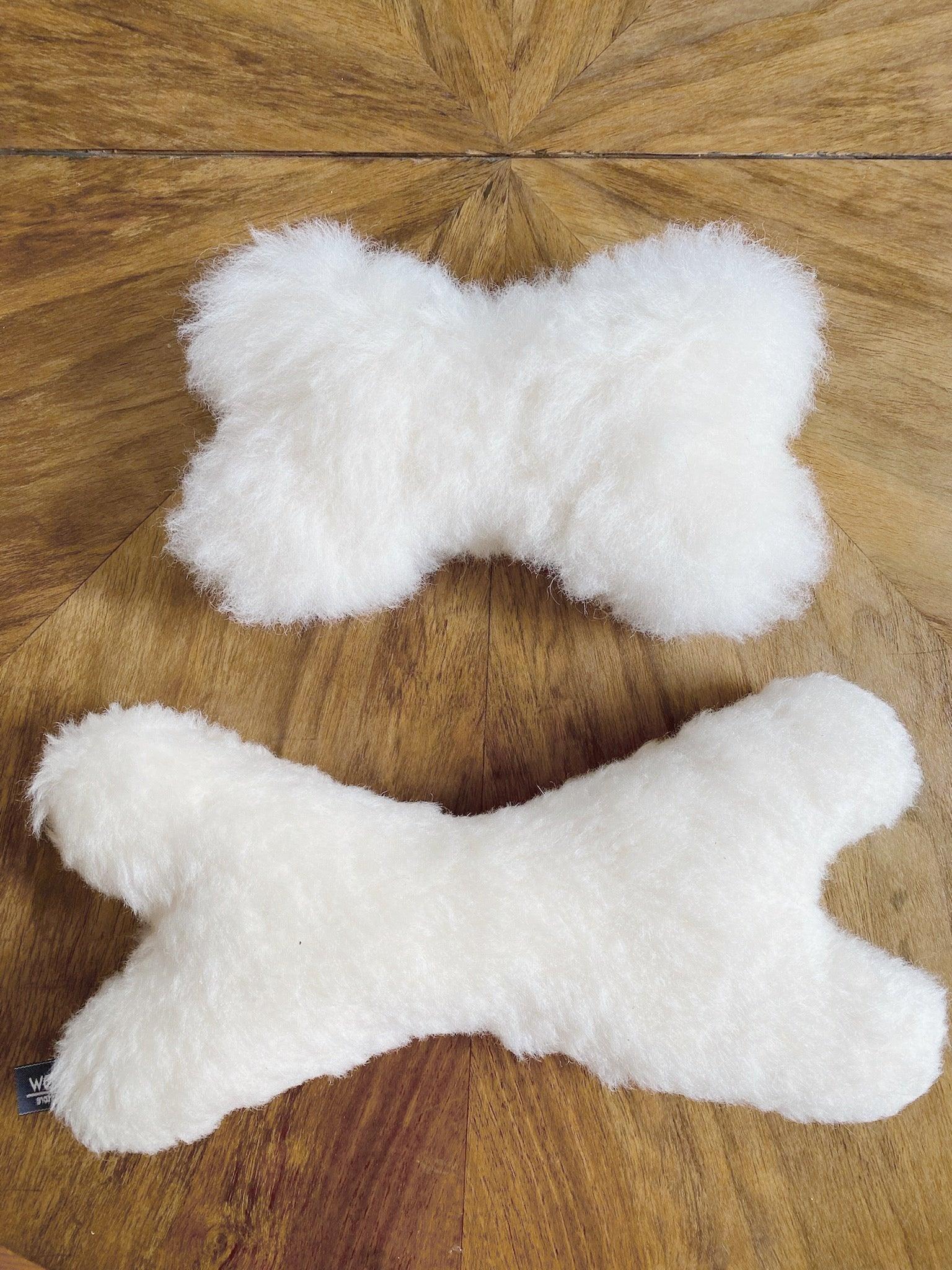 Two Natural Sheepskin Dog Toy Bones sit on a wooden table from Mellow Pet Store.